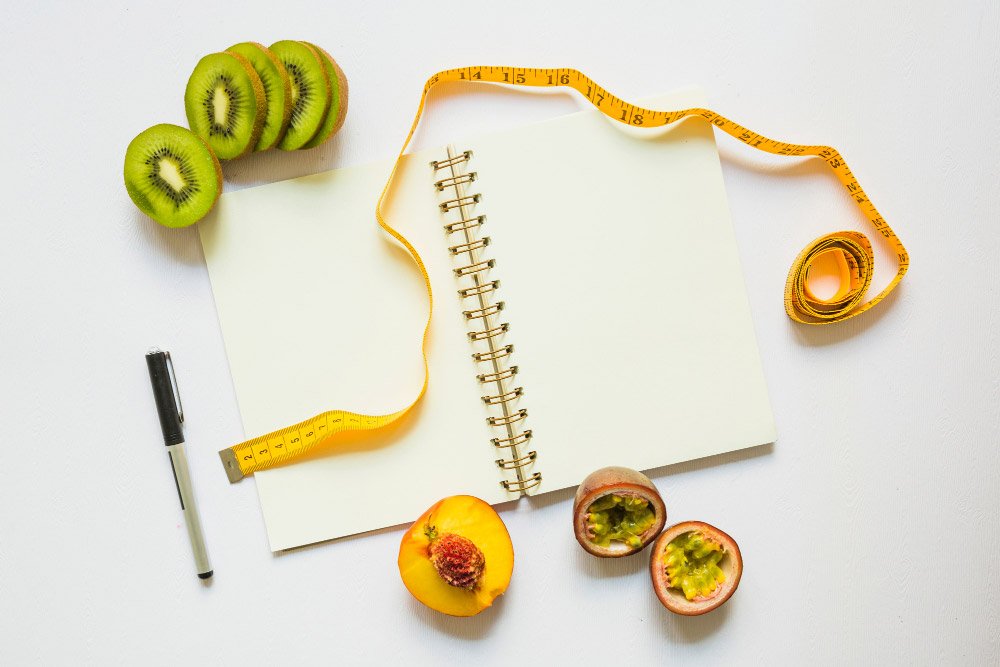 kiwi-slices-peach-passion-fruits-with-measuring-tape-pen-spiral-notebook