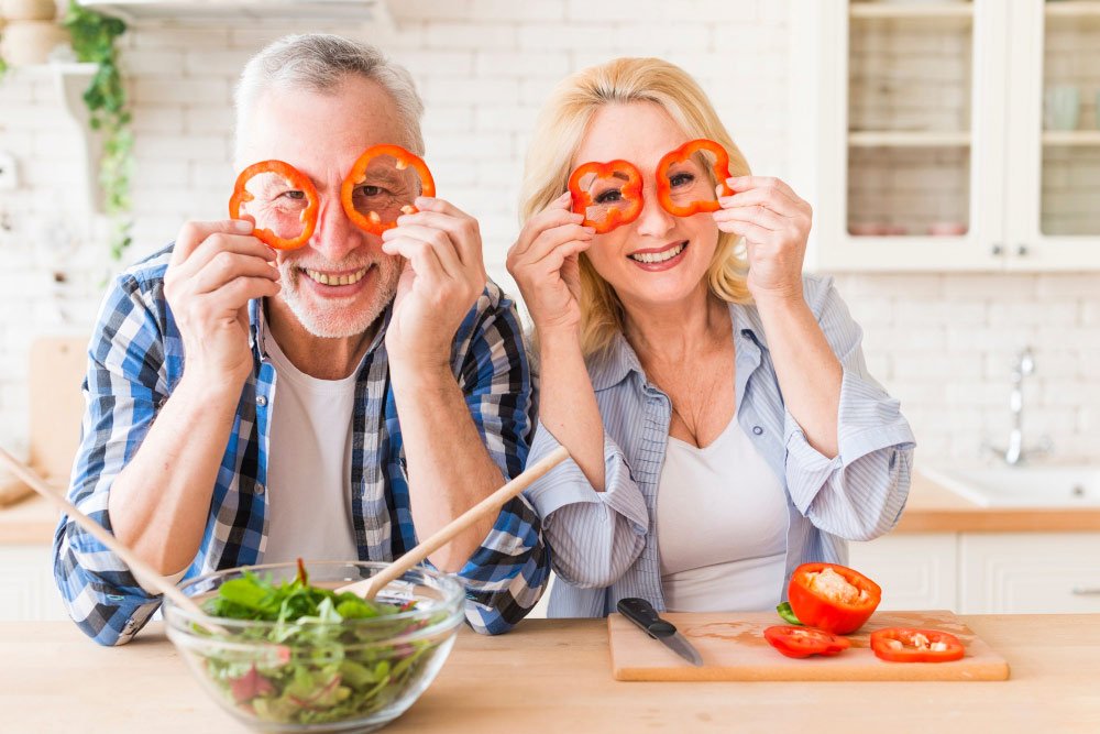 smiling-portrait-senior-couple-looking-through-red-bell-pepper-slice